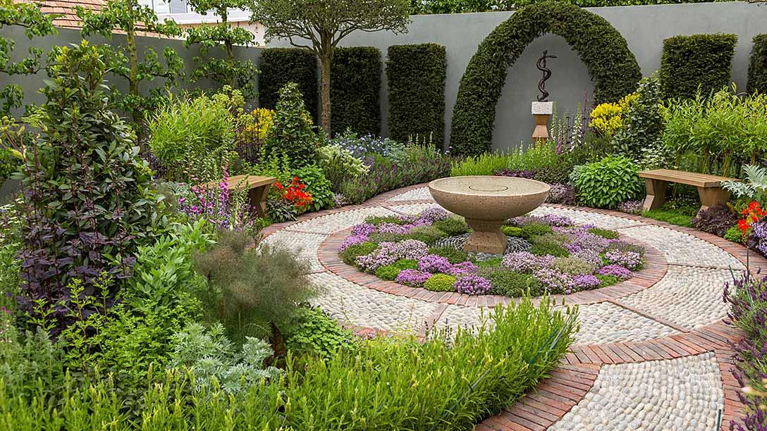 Reference view of a landscaped herbal garden with seating, planted beds and a central water feature
